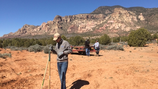 a person standing in a dirt field with a couple of people in the background